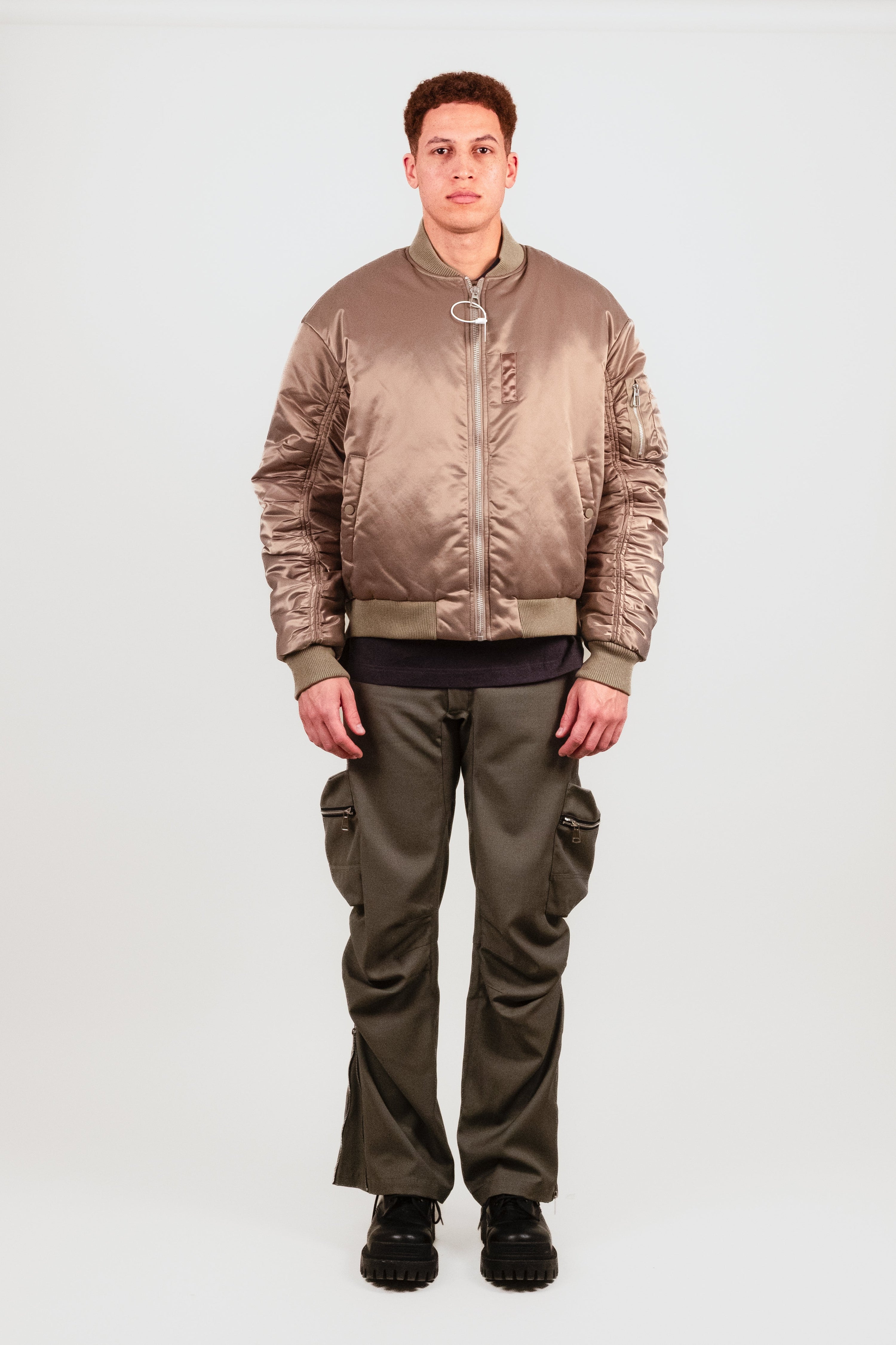 Nate wears the Ruched Bomber — olive green MA-1 style jacket with elegant sleeve ruching, heavyweight ribbing, and bright orange satin lining.