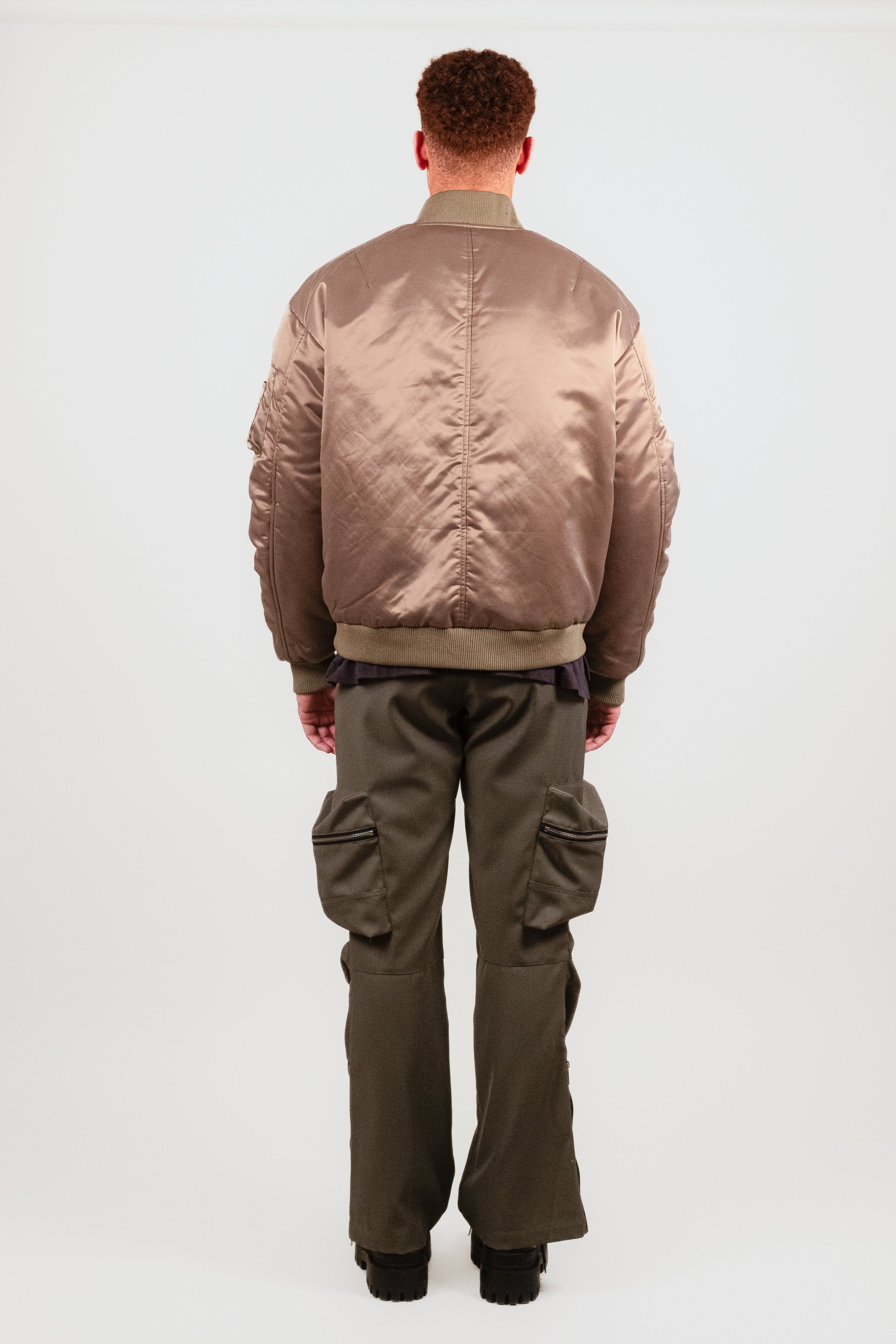 Back view of Nate in the Ruched Bomber — minimal streetwear silhouette with clean lines, ruched arms, and refined bomber proportions.