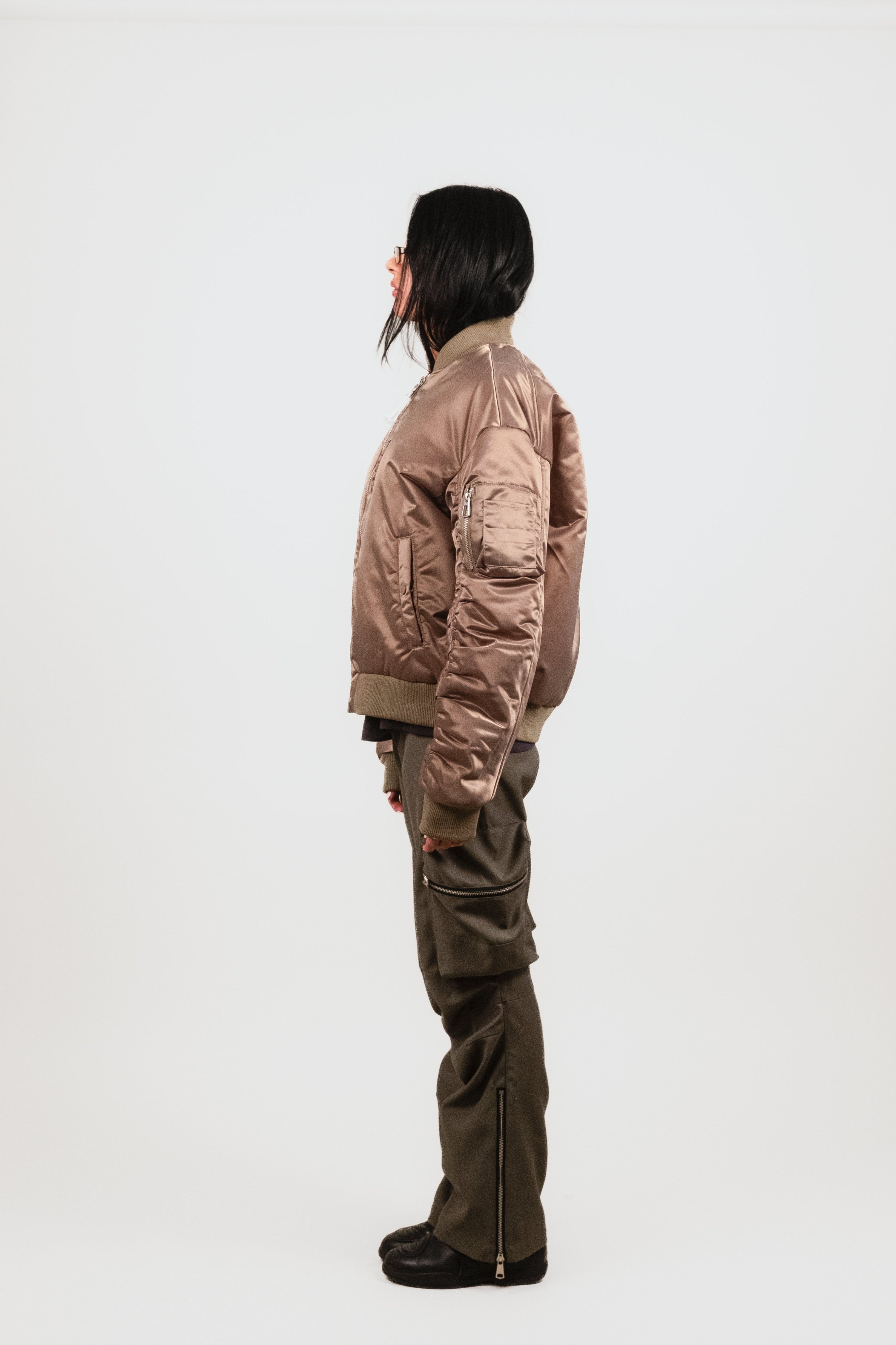 Profile view of Anisa in the Ruched Bomber — technical olive nylon bomber with tall ribbed collar and premium orange satin lining peeking from within.