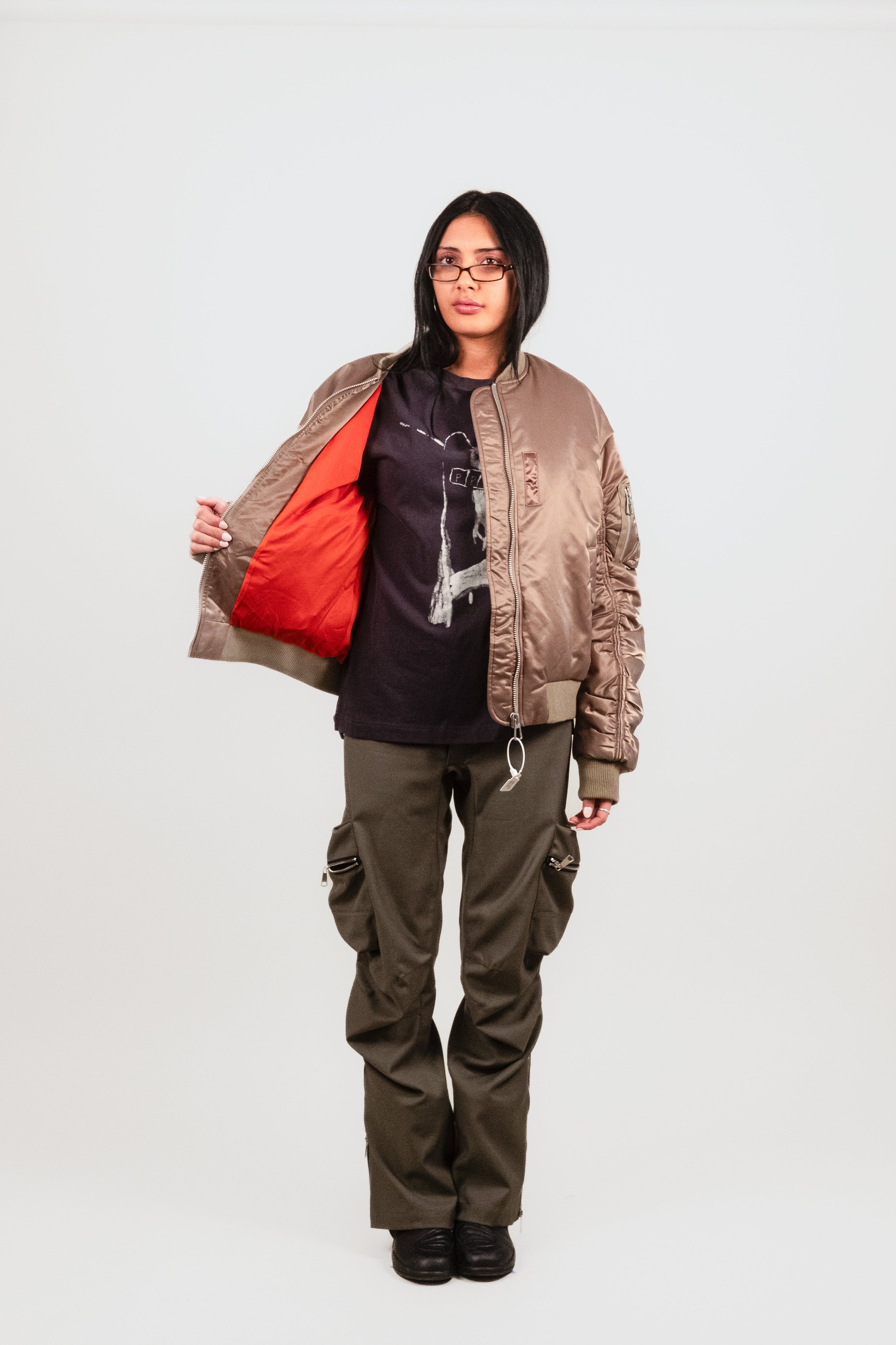 Alternate front facing photograph of Anisa wearing the Ruched Bomber — refined olive green nylon bomber with exaggerated ribbing and signature orange satin interior, being shown of here by Anisa.